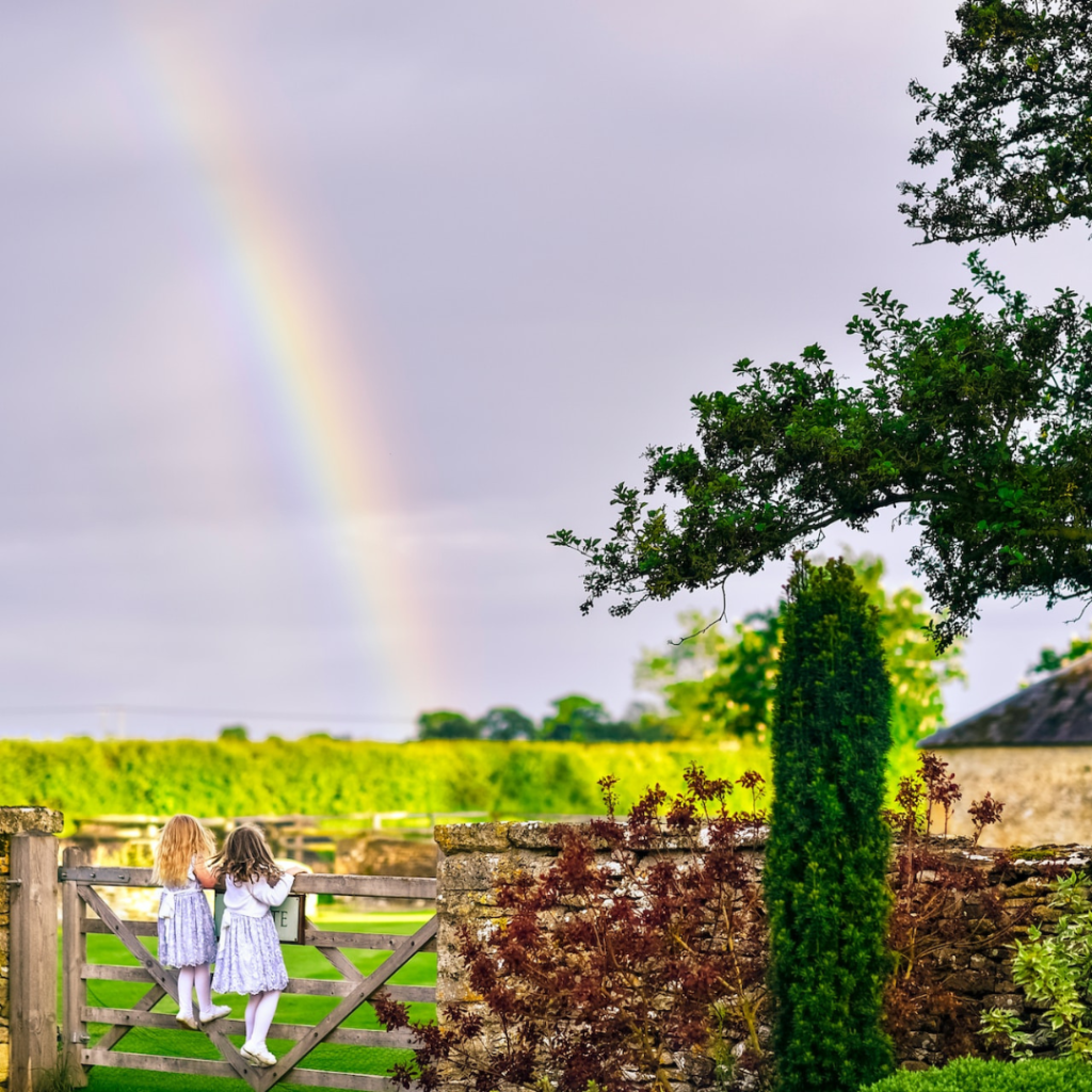 2 girls admiring sunshine and rainbows over a vineyard